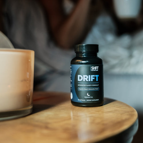 Bottle of DRIFT sleep supplement on a wooden bedside table next to a lit candle
